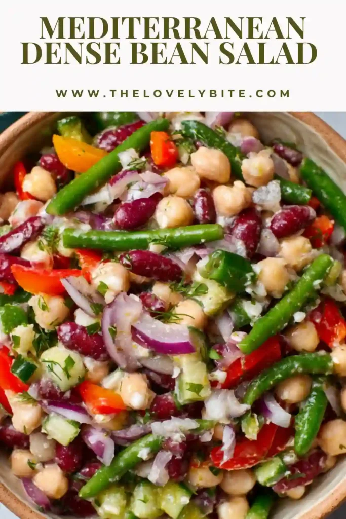A close-up of Mediterranean Dense Bean Salad served in a bowl, showing chickpeas, navy beans, cucumber, peppers, parsley, and creamy vegan feta. The texture looks hearty and satisfying with a glossy lemon garlic dressing.