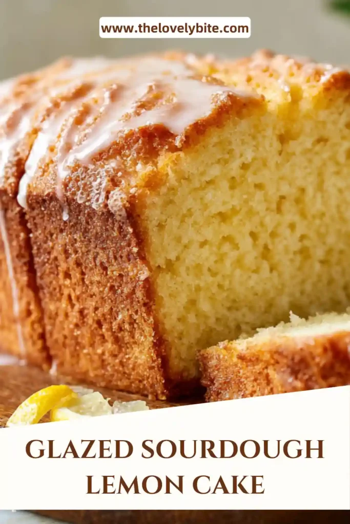 A glazed sourdough lemon cake sliced on a plate showing a moist crumb with a shiny lemon glaze on top. Fresh lemon zest is visible.