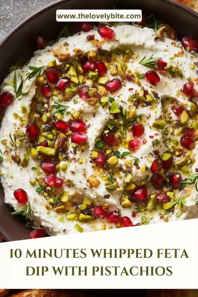 A creamy whipped feta dip with pistachios topped with pomegranate arils and drizzled with hot honey on a serving plate. The texture looks smooth with a slight crunch from nuts.