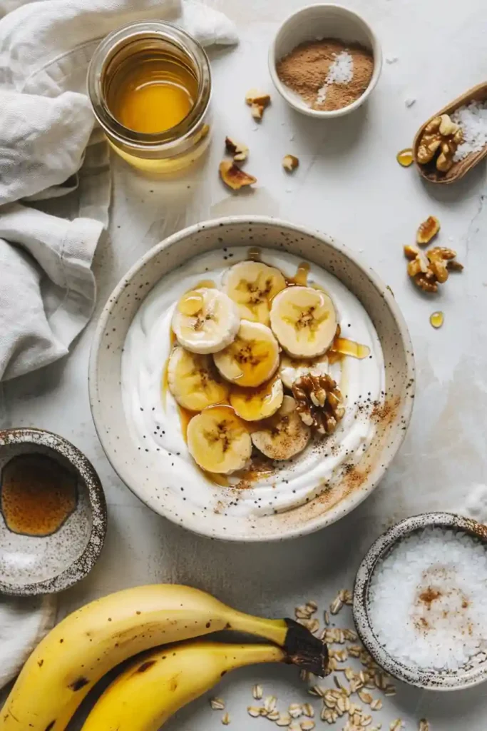 Healthy caramelized banana yogurt bowl served with toasted walnuts and peanut butter drizzle. The creamy Greek yogurt and warm bananas create a cozy high protein breakfast.
