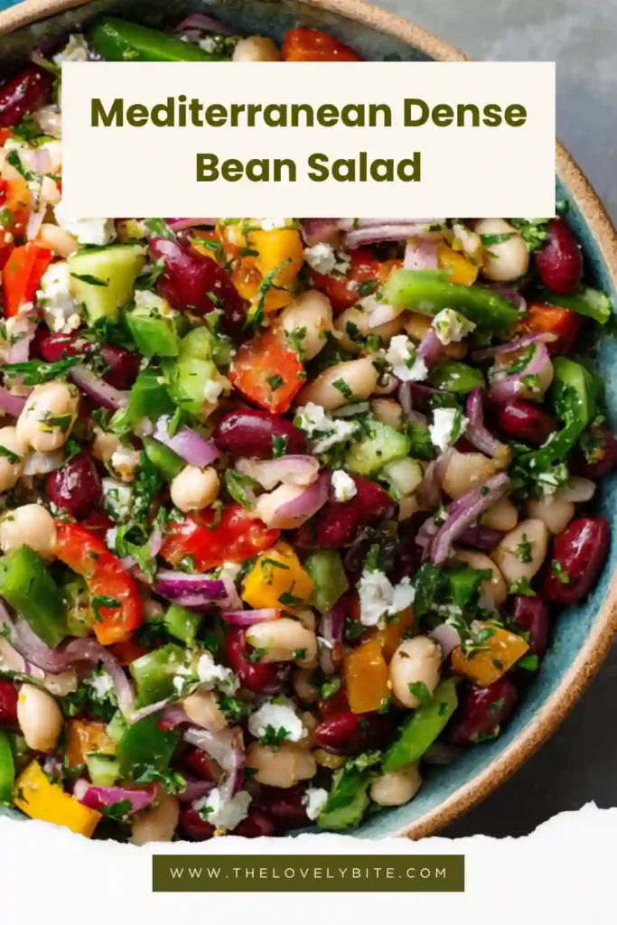 A bowl of Mediterranean Dense Bean Salad filled with chickpeas, navy beans, cucumbers, bell peppers, Kalamata olives, and vegan feta tossed in lemon herb dressing. This colorful Mediterranean salad is fresh, hearty, and perfect for meal prep.