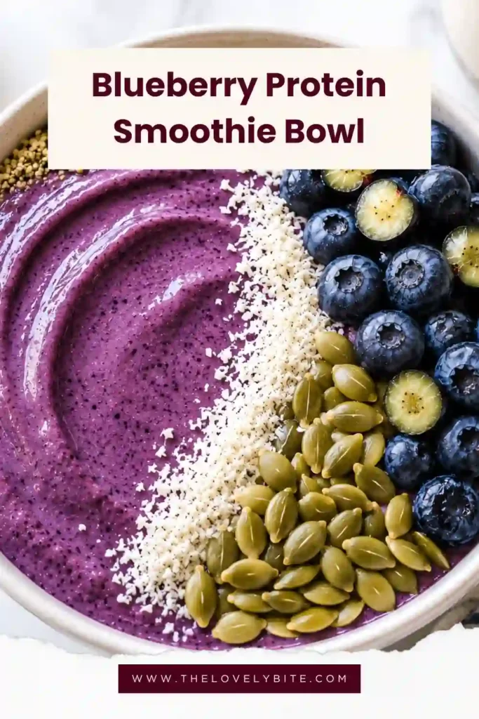 Thick blueberry protein smoothie blended with almond milk, avocado, and vanilla protein powder, finished with crunchy seeds and coconut for extra texture