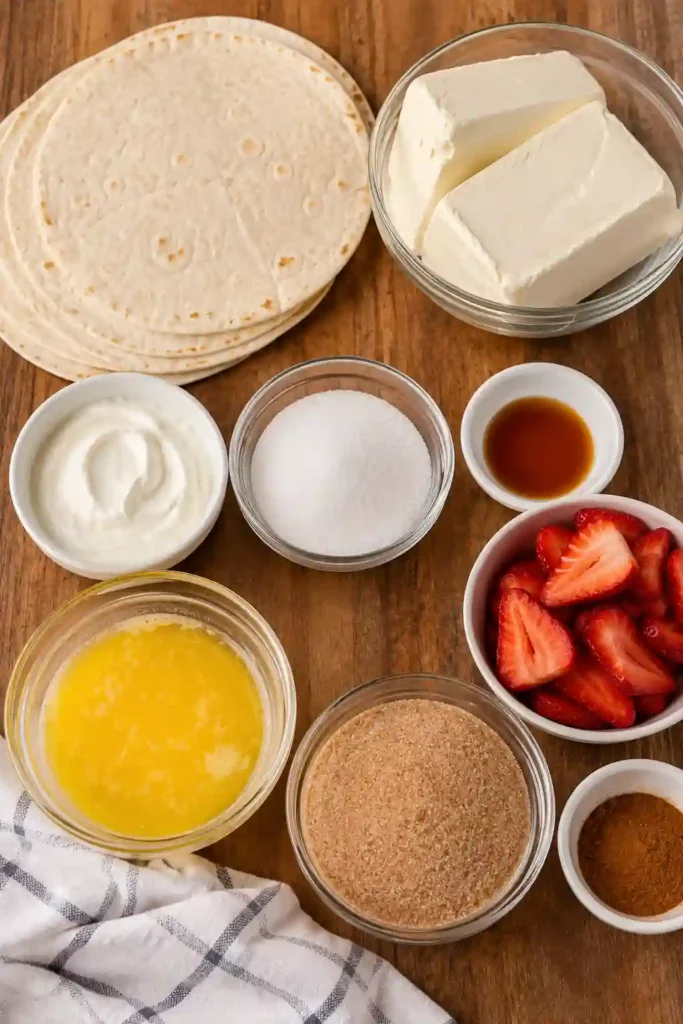A plate of baked Cheesecake Taquitos served with strawberries and caramel sauce. The golden tortillas are coated in a sweet cinnamon sugar mixture.