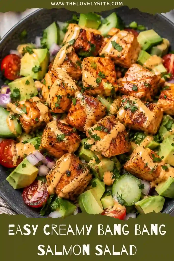 Healthy Creamy Bang Bang Salmon Salad served with fresh cucumber, red onion, tomatoes, and avocado. The salmon is perfectly cooked and drizzled with a creamy spicy dressing.