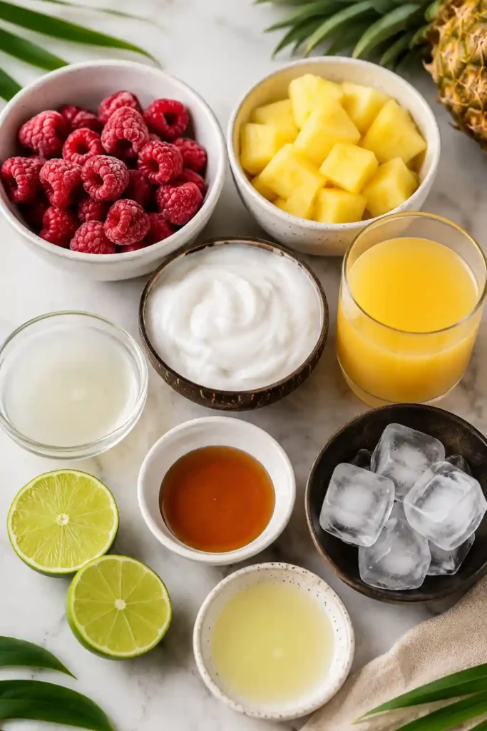 A chilled raspberry pineapple coconut drink served in a clear glass with tropical fruit decorations. The beverage has a rich, smooth consistency and vibrant appearance.