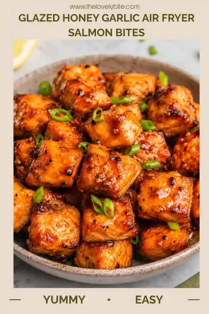Close-up of crispy air fryer salmon bites brushed with a sweet honey garlic sauce. Fresh lemon and herbs add vibrant color and flavor to the dish.