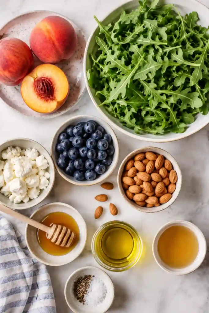 Healthy Grilled Peach Arugula Salad with fresh fruit, leafy greens, goat cheese, and crunchy almonds arranged in a large serving bowl. Perfect for summer gatherings and light lunches.