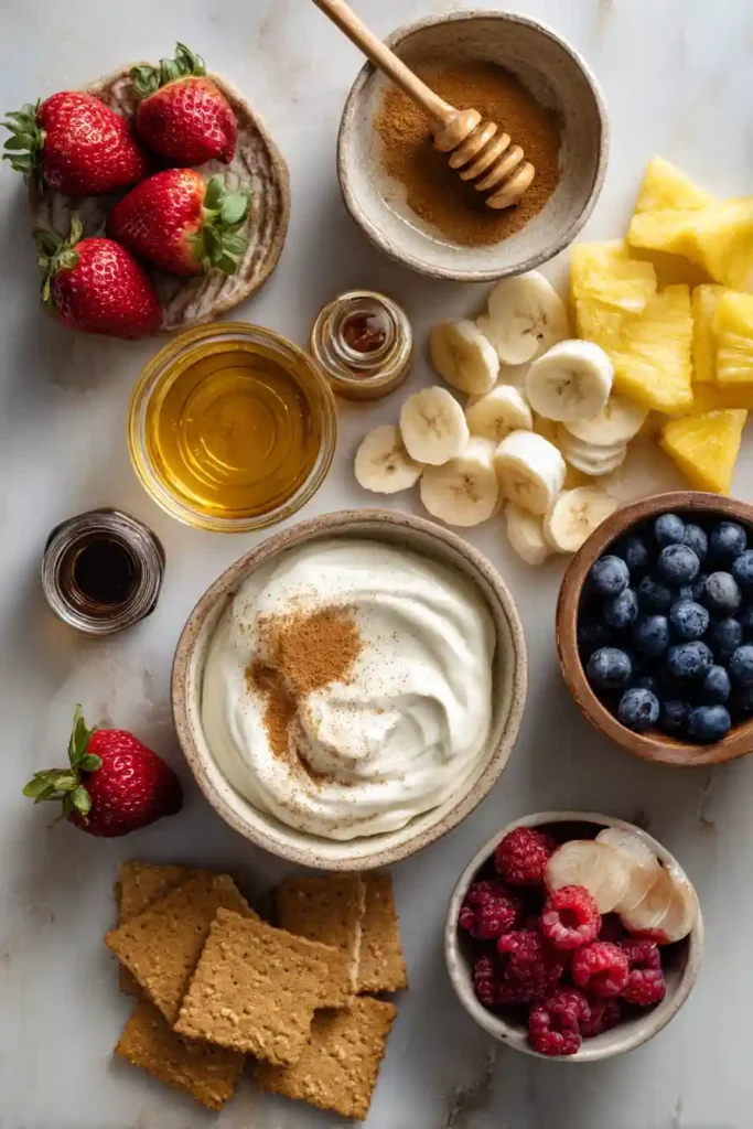 A bowl of Honey Cinnamon Greek Yogurt Fruit Dip served with fresh strawberries, grapes, and pineapple. This creamy high-protein fruit dip makes a healthy and delicious snack.
