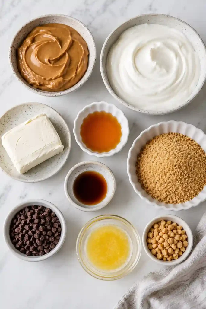 Peanut Butter Greek Yogurt Cheesecake Cups served in individual glass jars with a buttery graham cracker crust and chocolate drizzle. The creamy no-bake dessert is topped with chopped peanuts for extra crunch.