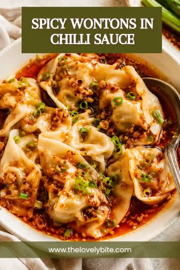 A bowl of Spicy Wontons in Chilli Sauce topped with chopped green onions and coated in glossy garlic chili oil. Tender dumplings sit in a rich, flavorful sauce with vibrant red chili flakes.