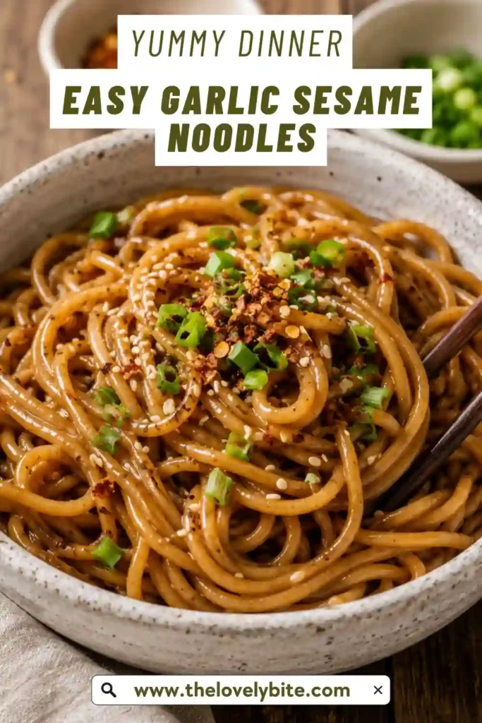 Garlic Sesame Noodles coated in a glossy tahini and toasted sesame oil sauce with fresh garlic and ginger. The noodles are topped with scallions, crushed peanuts, and red pepper flakes.