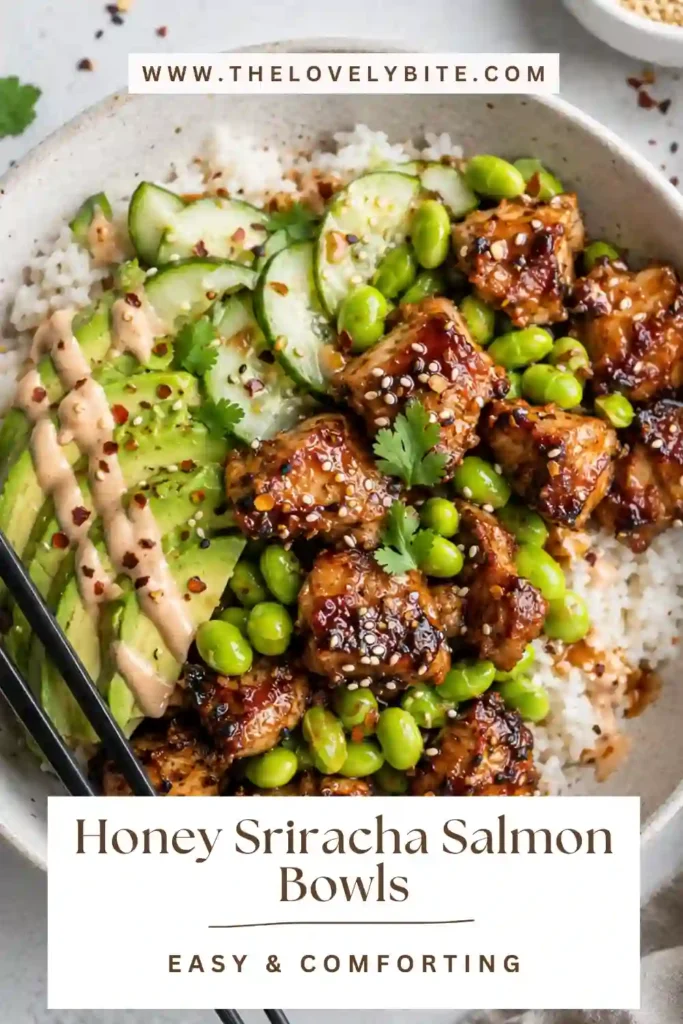 Spicy salmon bowls featuring honey sriracha salmon, white rice, avocado, cucumber, edamame, and creamy sriracha mayo. Sesame seeds and red pepper flakes finish the colorful bowl.