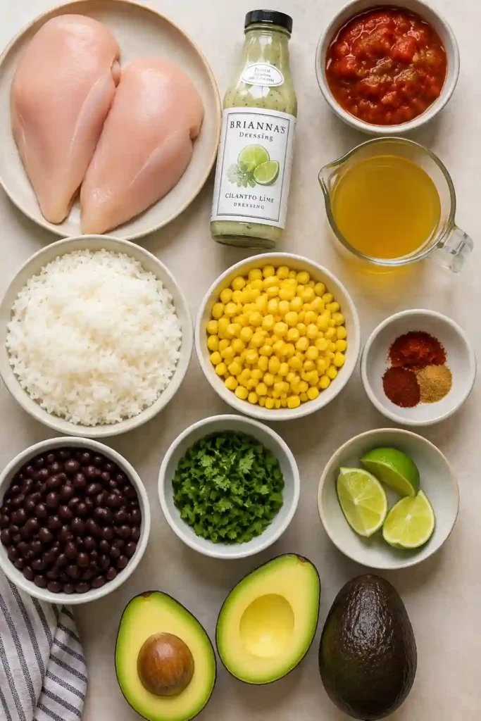 An easy burrito bowl topped with shredded Mexican chicken, black beans, sweet corn, diced avocado, fresh cilantro, and lime. A creamy cilantro lime dressing is drizzled over the colorful ingredients.