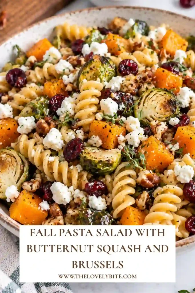Fall pasta salad with rotini, roasted butternut squash, Brussels sprouts, diced apples, goat cheese, and dried cranberries in a serving bowl. The colorful autumn ingredients are coated in maple Dijon dressing.