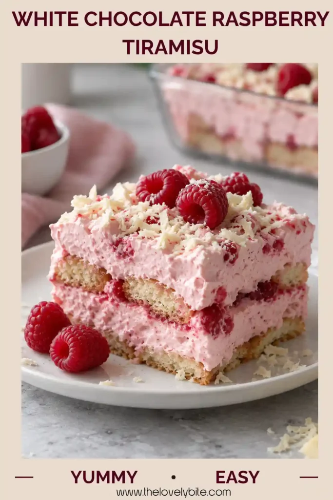 A square serving of White Chocolate Raspberry Tiramisu topped with delicate white chocolate shavings. The raspberry dessert features creamy mascarpone layers and soft, berry-infused ladyfingers.